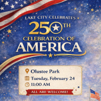 Gazeebo with grassy field. American flag. Light pole. City of Lake City and Columbia County logos.