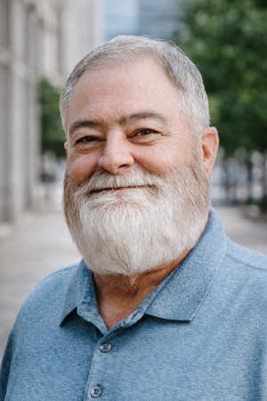 Man with short, gray hair, a full beard, and a blue collared shirt.