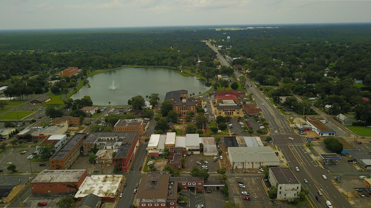 Downtown Lake City.  The lake with fountain in the back ground, several roof tops and the busy W Duval Street to the right.  